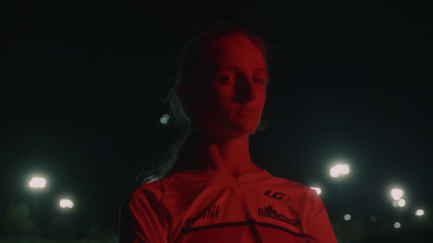 Young teenage girl under a red light looking at the camera standing outdoors at night