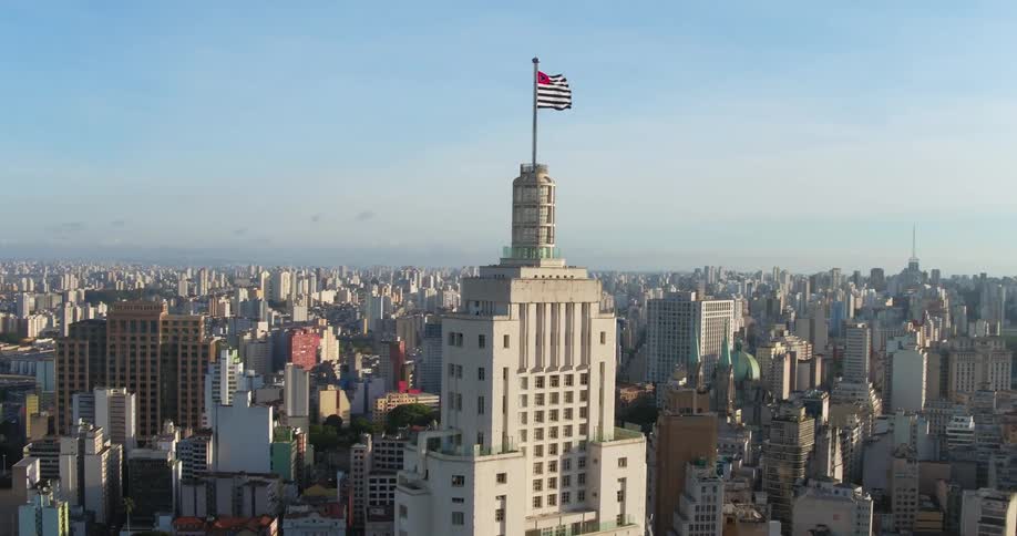 A large flag flies on top of a tall skyscraper