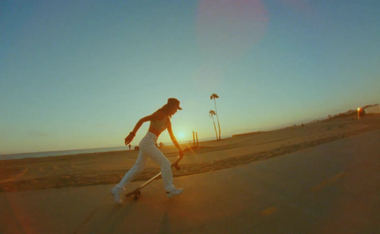 Young woman rides a skateboard on a road in the beach next to the ocean caught on vintage film