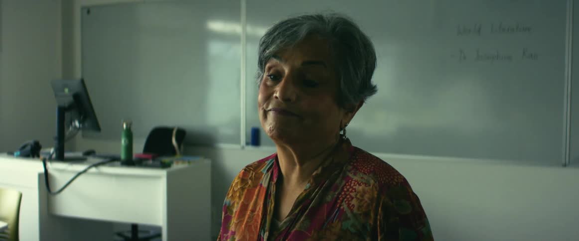 A teacher stands alone in her classroom thinking about something that seems to be making her sad