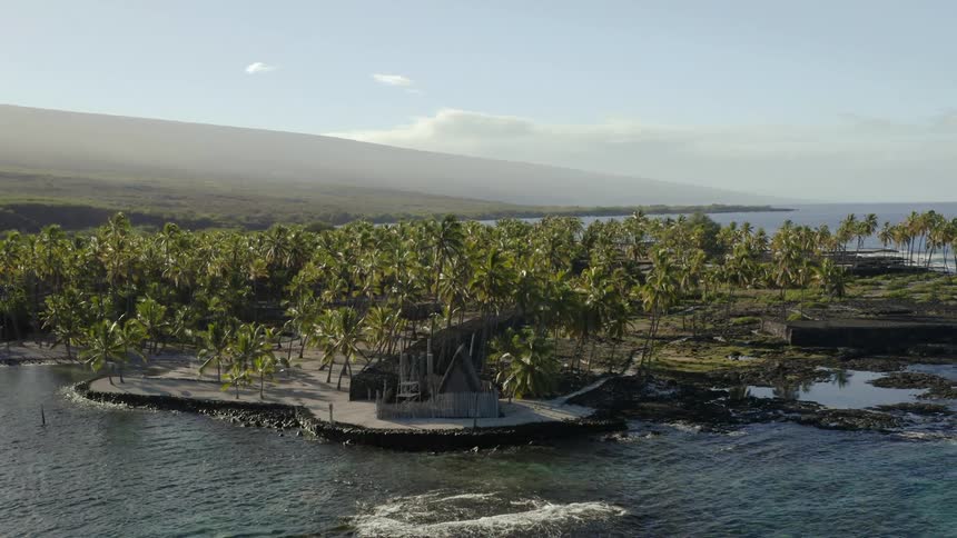 A house sits on the coast of an island that is near land with mountains