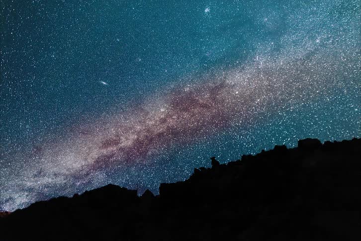 Time lapse of a colorful galaxy moving over the silhouette of a mountain range at night