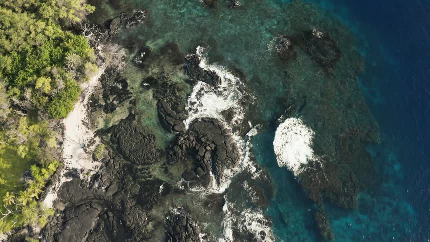 Ocean waves splashing against a rocky shore with turquoise water turning deep blue