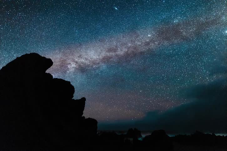 The milky way along with a sky filled with stars shines in the sky near a cliff