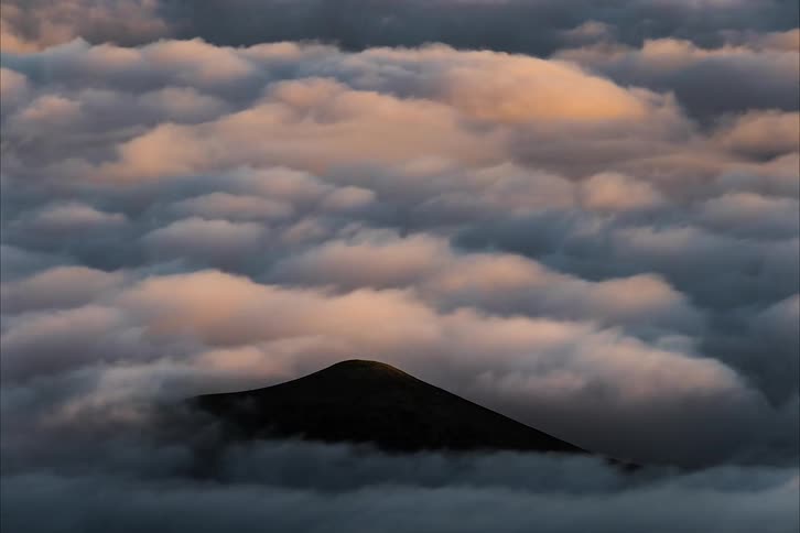 A mountain peak sticking up above rolling clouds from day to dusk