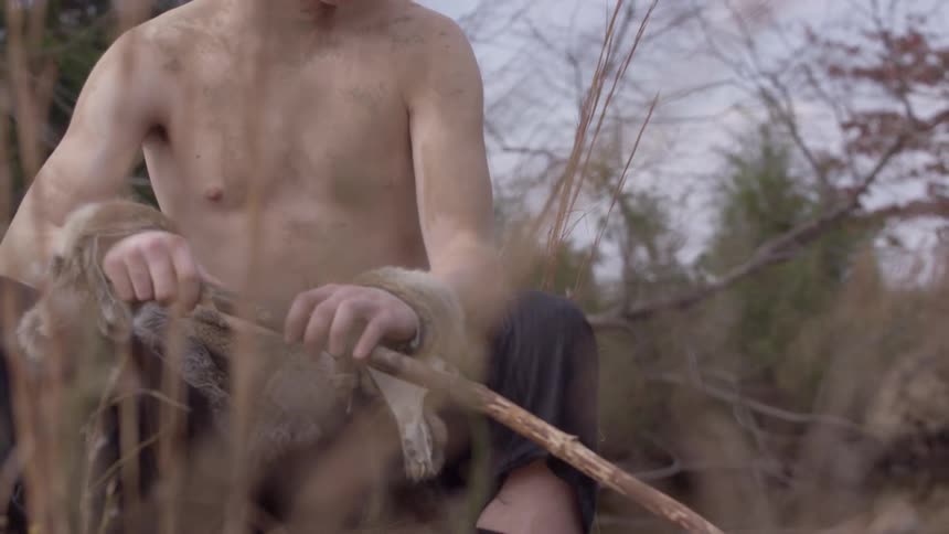 A shirtless young man stirs water in a lake with a long stick