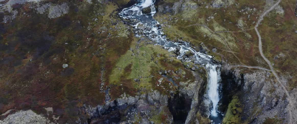 Rushing river water flows down the slope of a mountain and over a cliff in a waterfall
