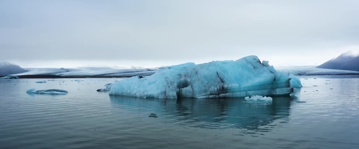 A large piece of ice floating in the water with surface rippling under a cloudy sky