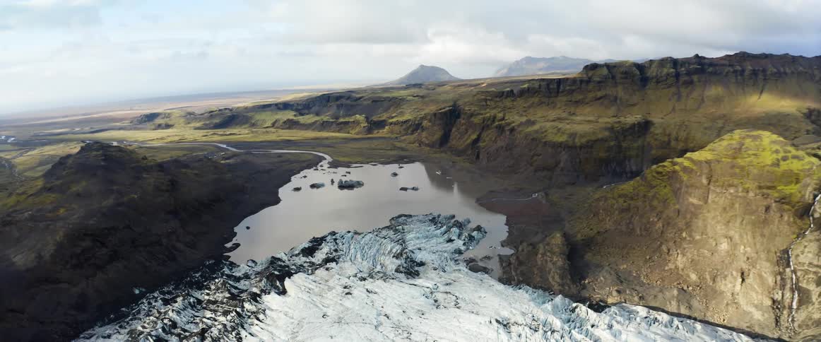 A smooth lake with icebergs floating at the base of a glacier and cliffs