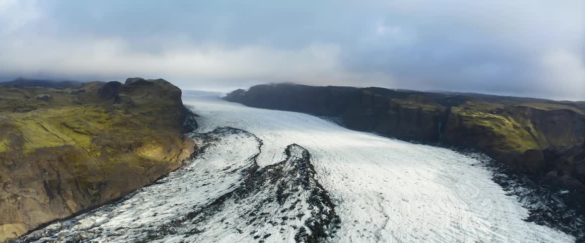 Aerial view of a glacier moving down a valley between mountains reaching the ocean
