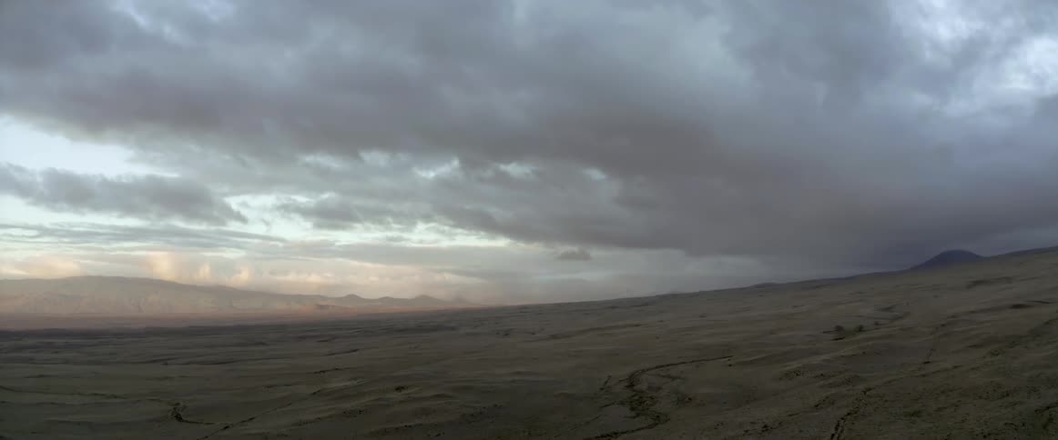 Clouds hanging over the barren terrain near the mountains at evening