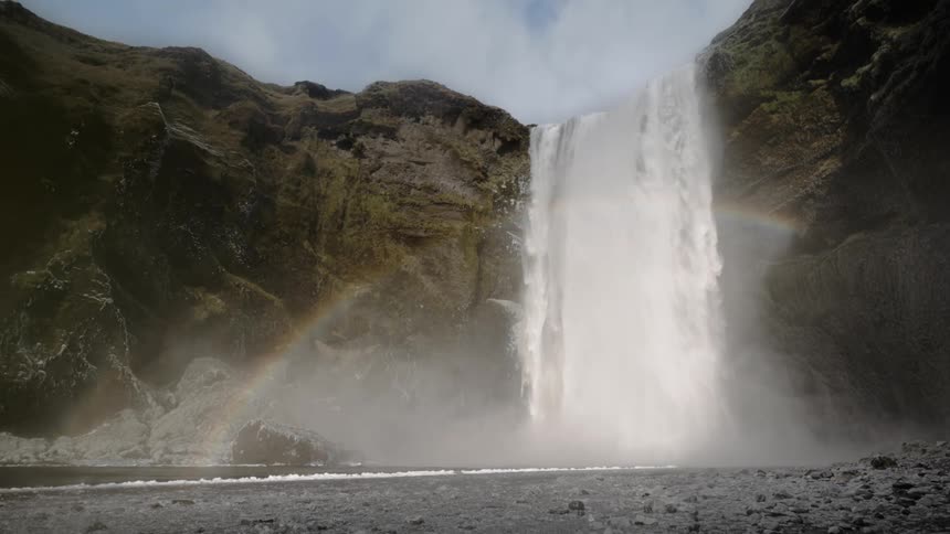 A rainbow appears near a large waterfall and river