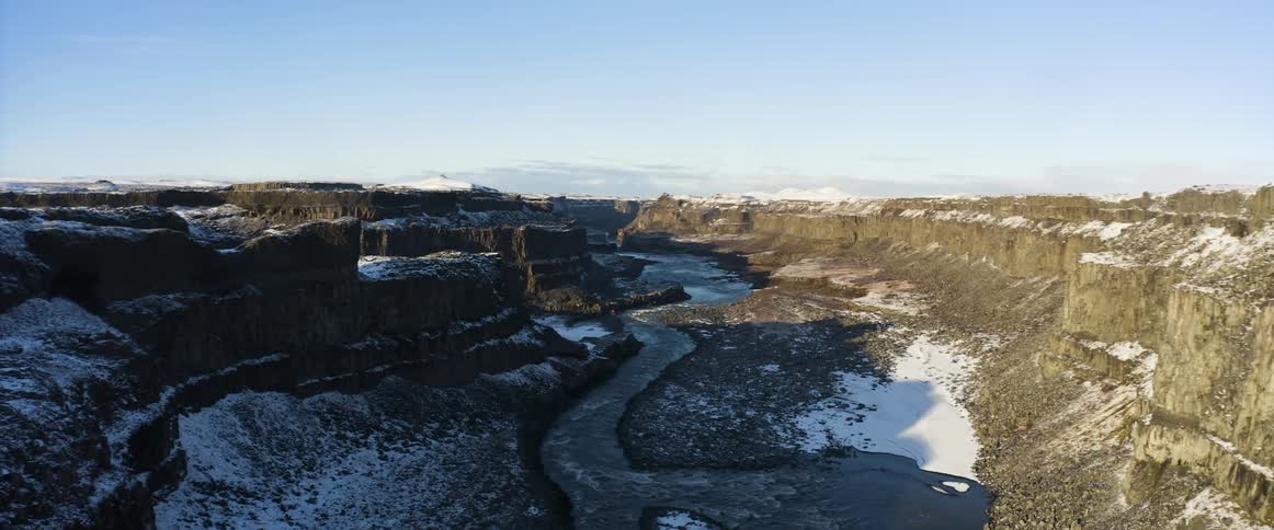 Aerial view of a river flowing through a narrow canyon in the snow covered mountains at morning