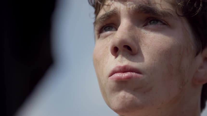 A dirty young man looks upwards while standing outside in the daytime