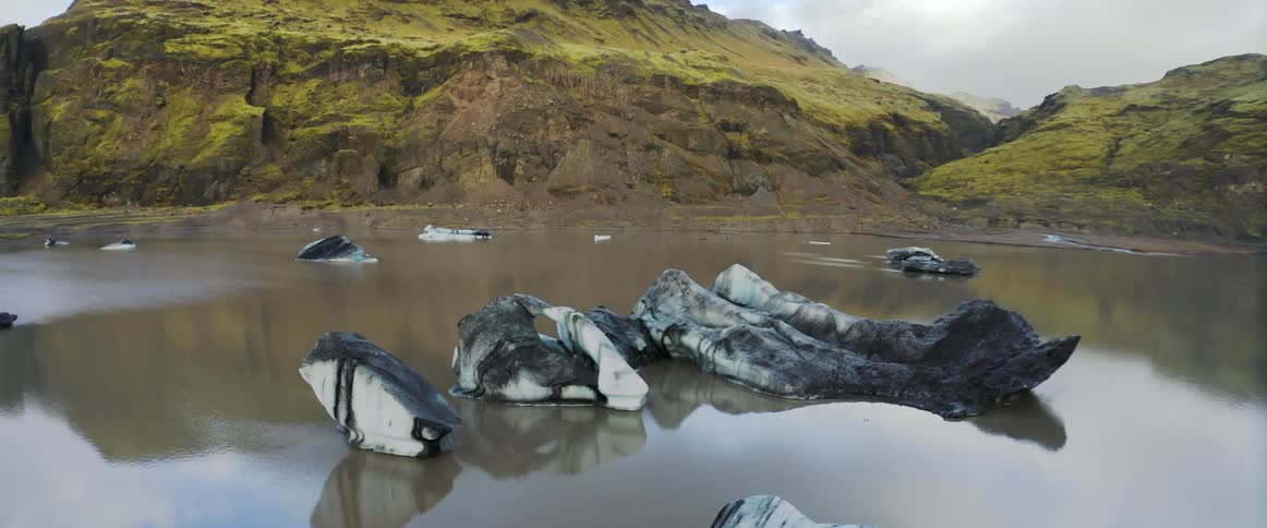 Ice floats on reflective water near lichen covered cliffs