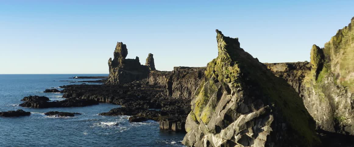 Steep cliffs are on the shoreline of an ocean that has small rocky islands just off the coast