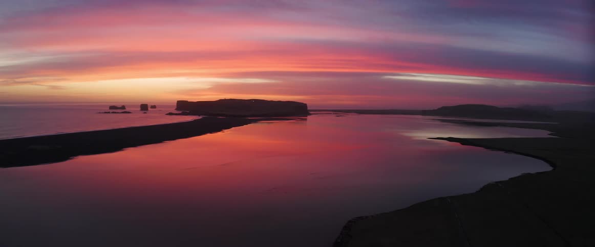 Ocean waves lap against rock formations while the surface reflects the brilliant colorful sunset
