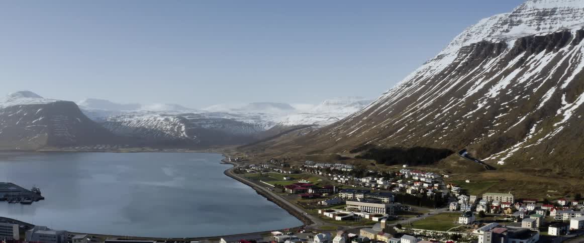 Aerial view of a small coastal town at the base of a tall mountain range covered in snow
