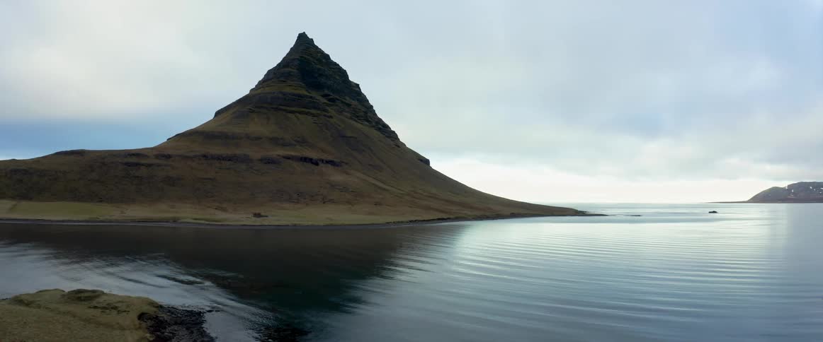 Water rippling off a coastline with a mountain peak in the distance