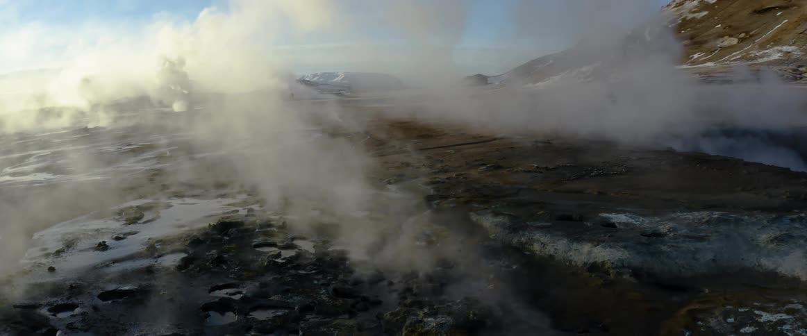 Steam rises from natural thermal vents on the ground near the mountains at sunset