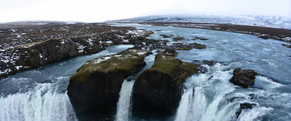 Aerial view of a wide waterfall streaming down the rocky plains next to the mountains