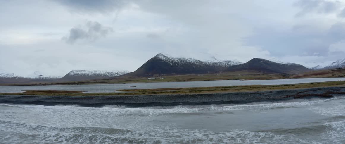 Ocean waves washing ashore a shoreline with snowy mountains in the distance