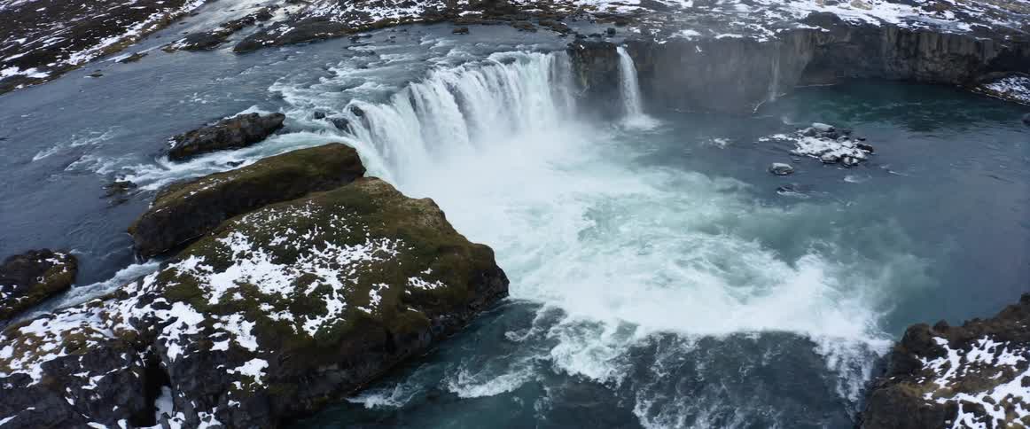 Large rocks are covered in ice in a river that has a waterfall