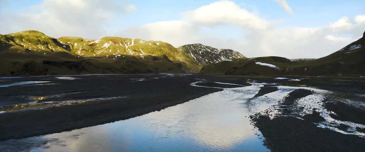 A drone in the air films a landscape of hills and mountains and over water and asphalt