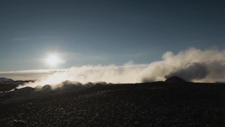 Steam rises from thermal vents near gravel covered terrain under a bright sun