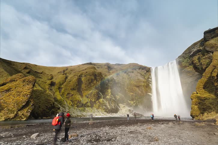 Time lapse of tourists visiting a waterfall next to the mountains