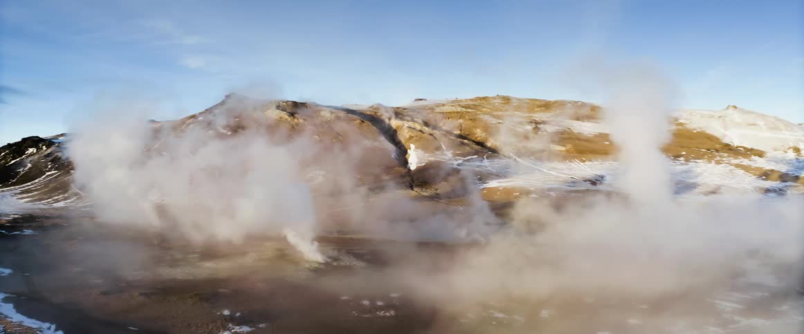 Smoke rises from geysers at the base of a canyon