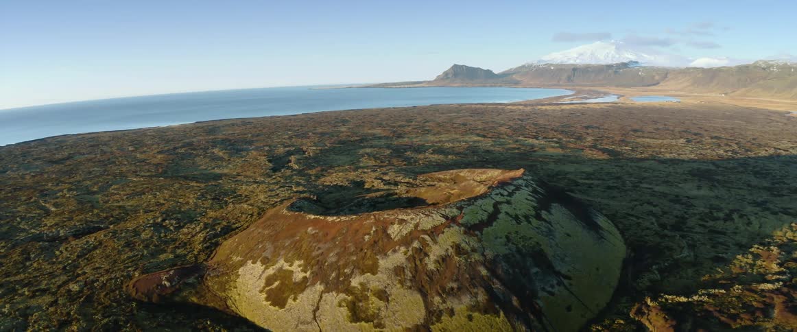 Crater sits in ground with ocean in the background and mountains on the horizon