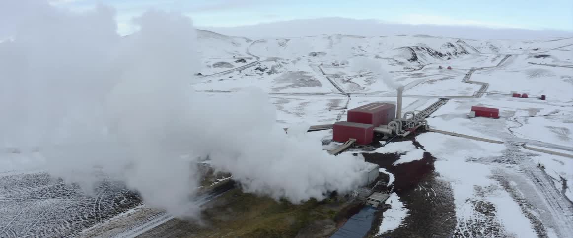Smoke and steam rise from manufacturing plant surrounded by snow covered fields