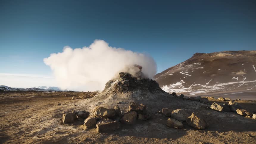 Smoke and steam billowing out of a geyser under a deep blue sky
