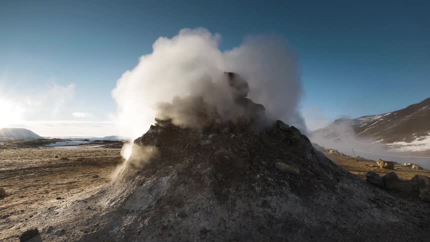 Steam rises from natural thermal vents on the ground near the mountains at sunset