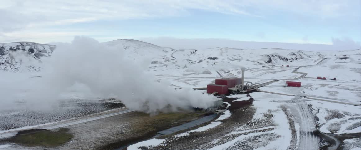 Camera tracks past factory or plant with large plume of smoke rising from it