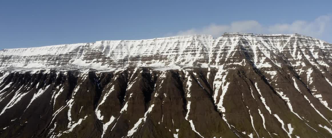 Snow is on the top of a mountain and runs down in crevices on the sides