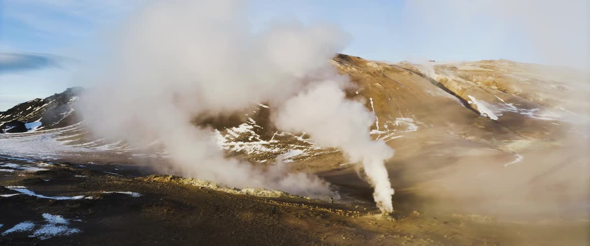 Vapor rises from snow dappled ground near base of a mountain