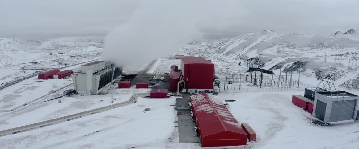 Aerial view of a the red buildings of a geothermal energy power plant on the plains covered in snow