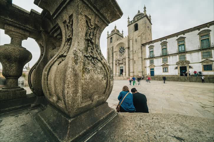 A couple sitting on the steps across from the porto cathedral hugging and taking selfies
