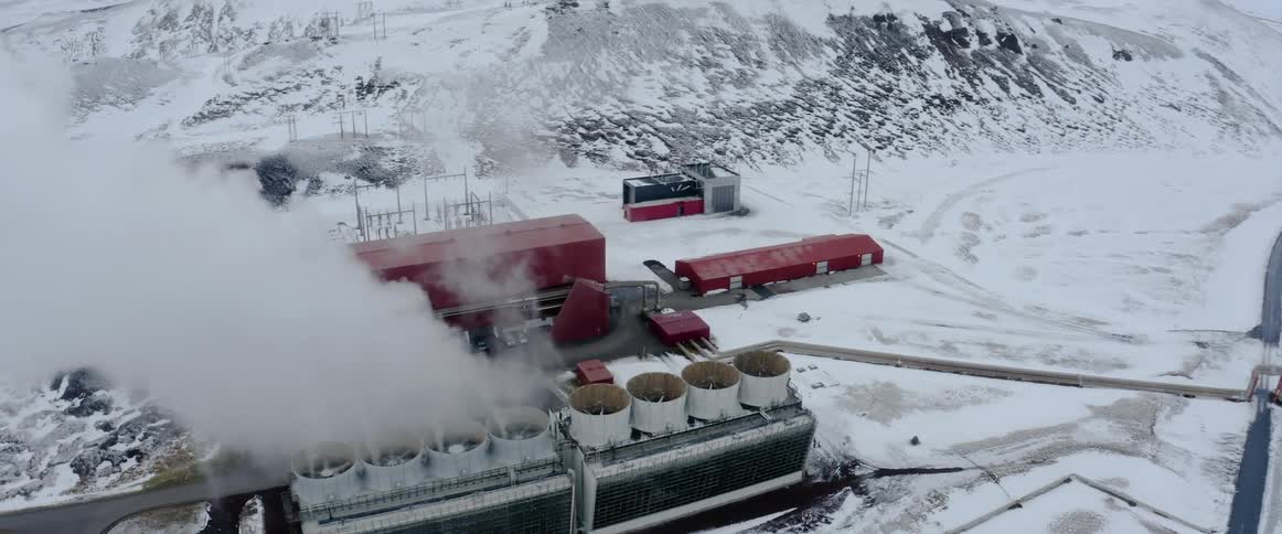 Smoke billows from a factory in a wintry countryside during the day