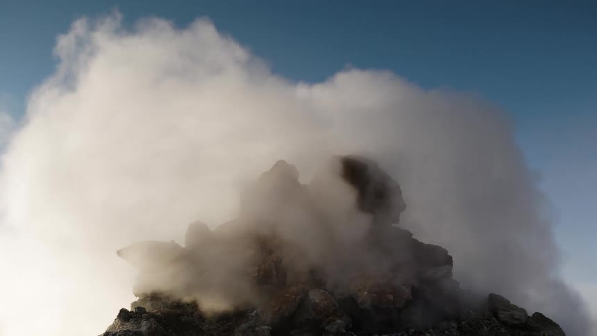 A volcano is spouting steam from the top of the peak