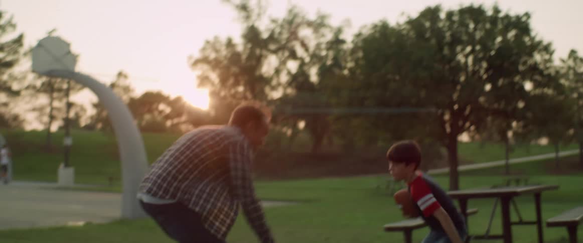 Father and son play football in park as others move about park in the back