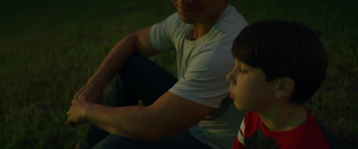 Dad smiles at his son as they both sit in the grass at night