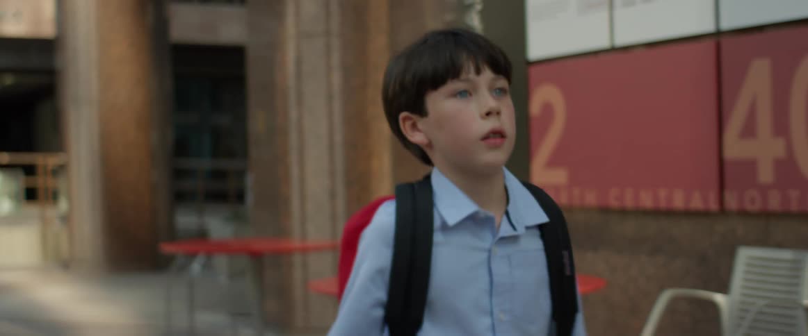 Young boy carrying a backpack walks near a building in the city at daytime