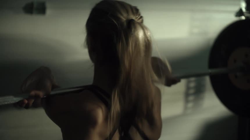 Blonde woman lifting a weighted gym barbell off the floor