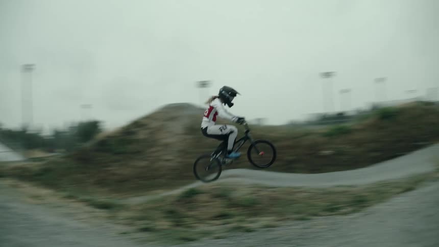 Woman on bmx bicycle course goes over hills and jumps