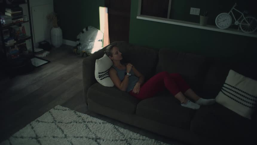 Woman reclines on sofa in dimly lit living room