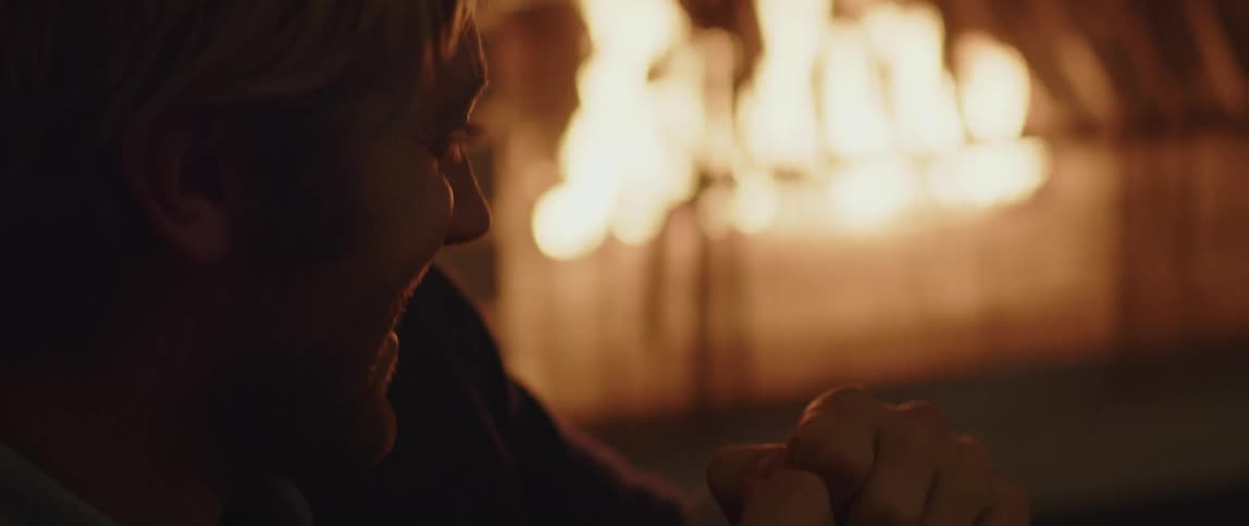 A man smiling and sitting by a fire in a fire place
