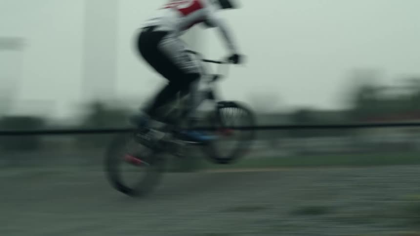 Person rides a motocross bicycle at full speed on a gravel track on an overcast day